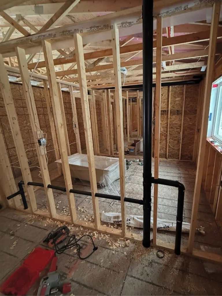 Bathroom plumbing rough-in in open framing on a Concepts Plumbing job — ABS drains and vent stack in place before the walls close